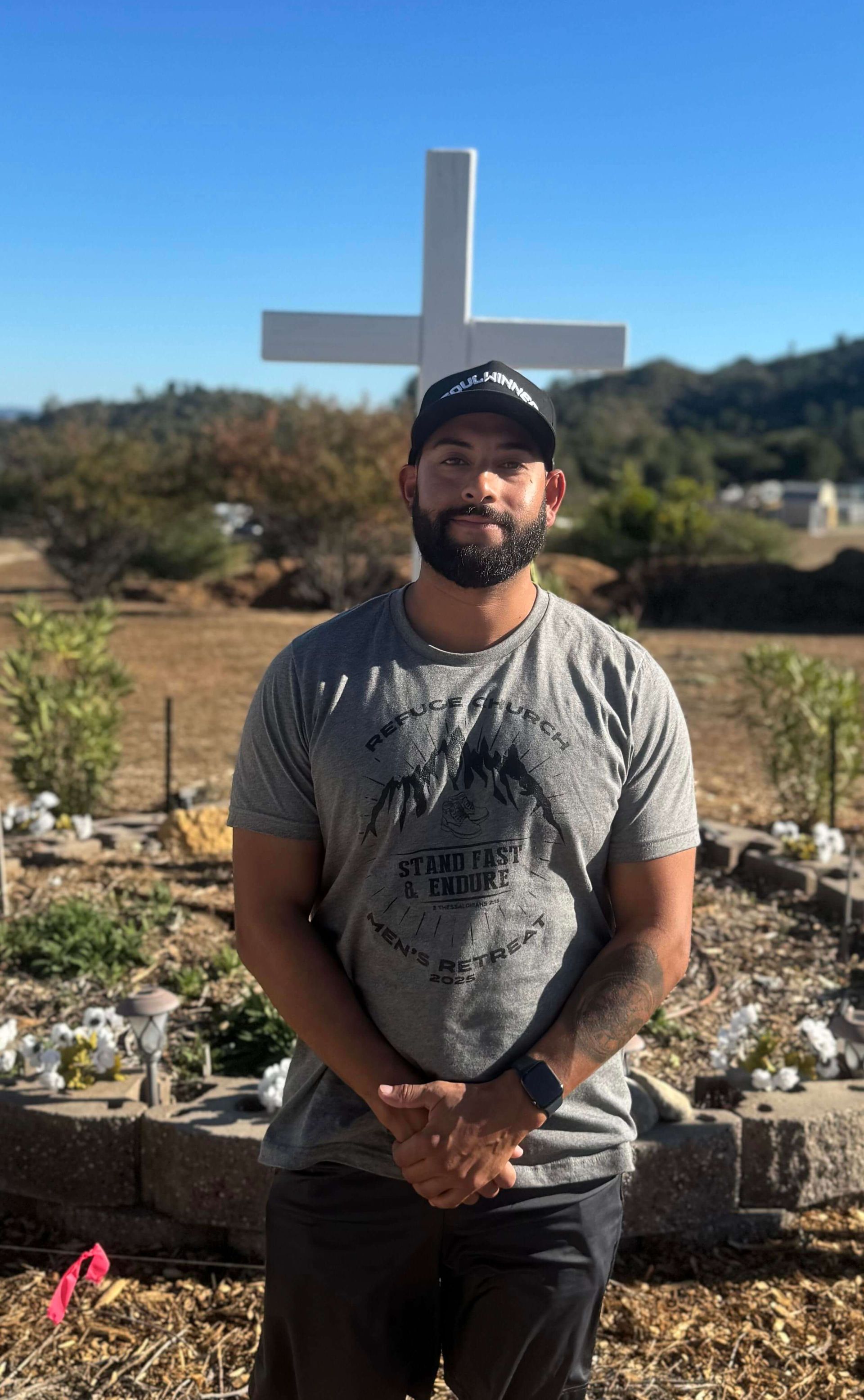 A man standing in front of a white cross on a sunny hillside