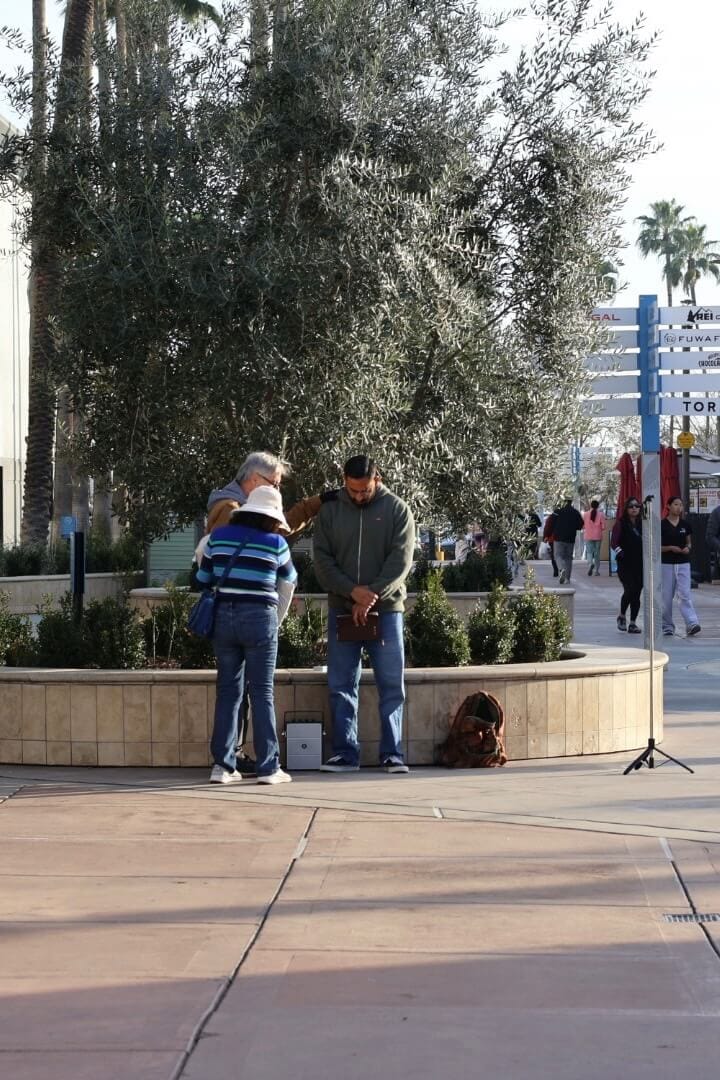 People gathered by a tree on a city sidewalk