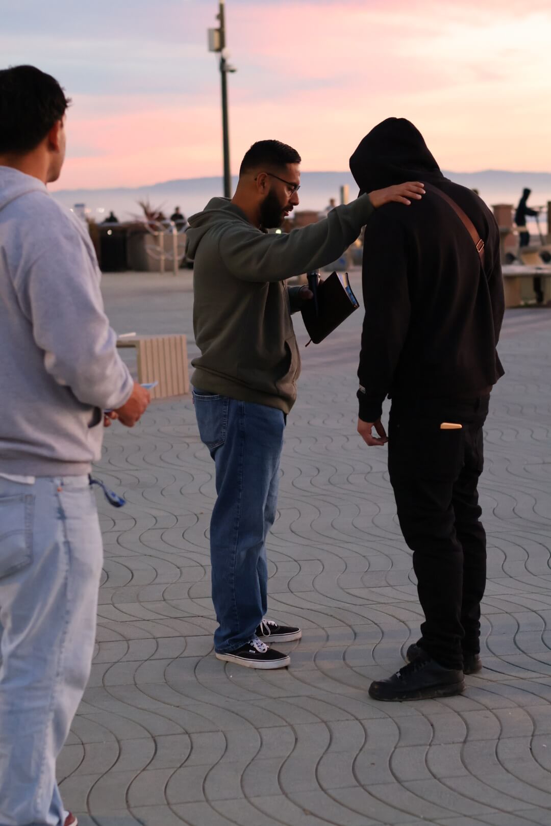 Joshua Maez praying with a young man on the boardwalk at sunset