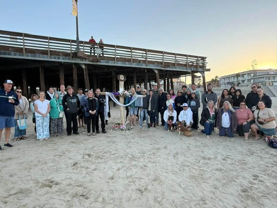 Beach memorial gathering under the pier at sunset